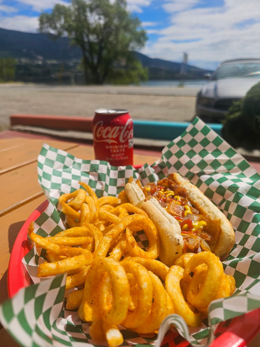 An all-beef dog from the grill with Wood Lake behind the picnic table